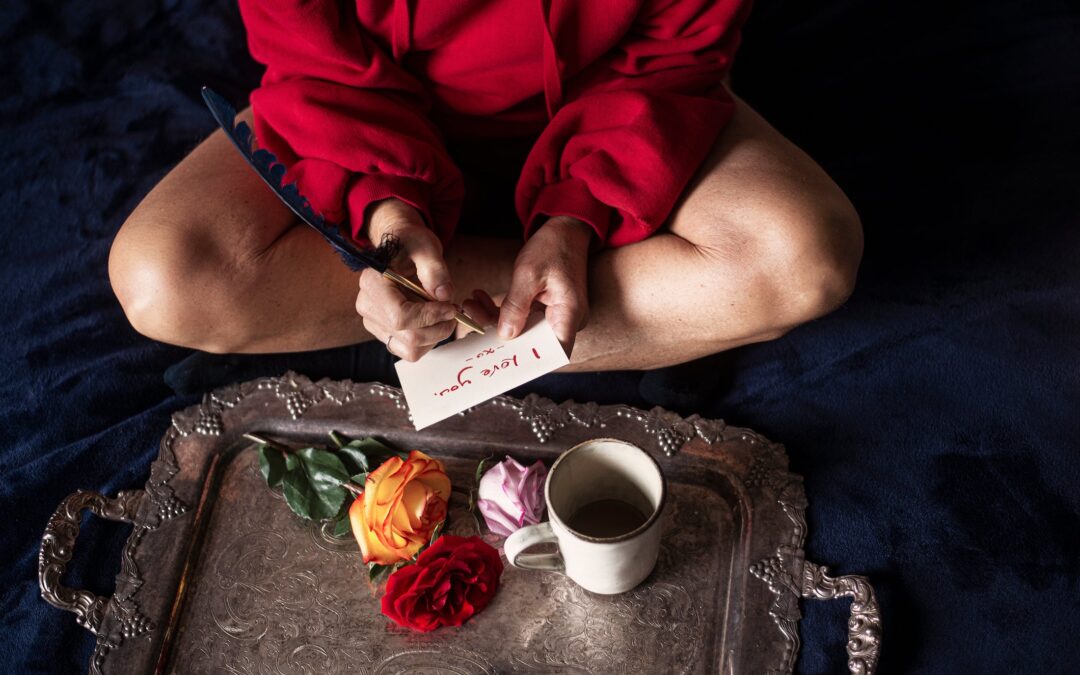 Woman in red writing "I love you" on postcard. Blog - How your period can affect fertility. Womb support.